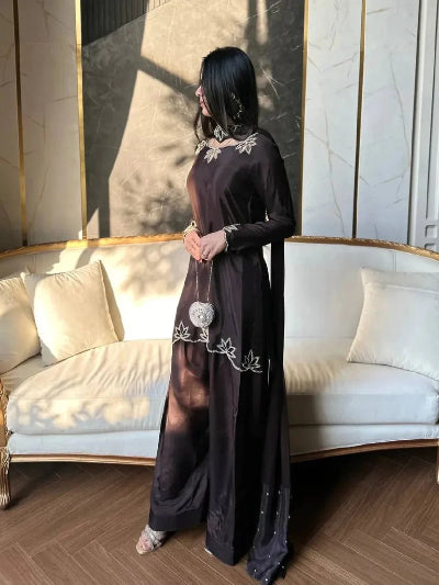Woman in a long black dress with white embroidery standing in a stylish room.