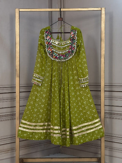 An olive green long kurta with white floral prints, gold zari borders, and a heavily embroidered multicolor neckline, hanging on a wooden hanger inside a gold metal clothing rack.Navratri Bandhani Kutchi Work Kurti UK | Garba Dress