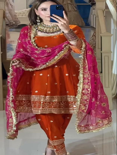 Woman in traditional orange and pink outfit with jewelry, taking a mirror selfie.