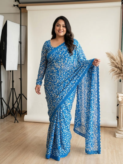 A woman modeling a bright blue floral printed saree with a matching blouse in a studio setting with a white backdrop and softbox lights.