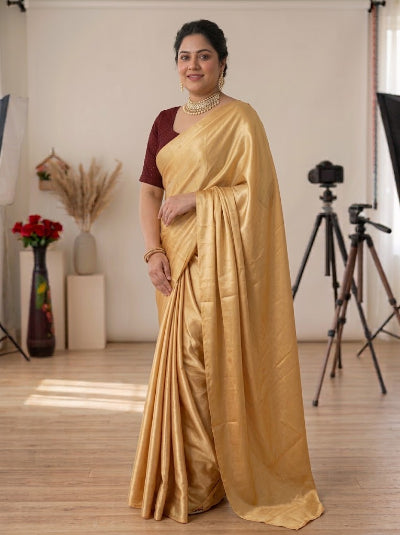 A woman modeling a golden yellow silk saree with a deep maroon sleeve, standing in a studio with photography equipment visible in the background.