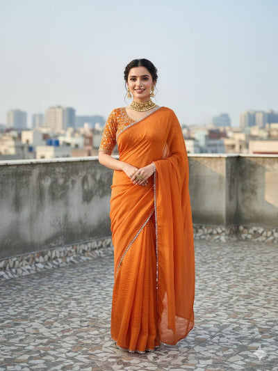 Woman in an orange saree standing on a rooftop with a cityscape in the background
