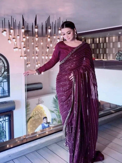 Woman in a maroon saree standing indoors with decorative elements in the background