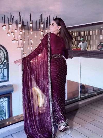 Woman in a maroon saree standing indoors with decorative chandelier in the background