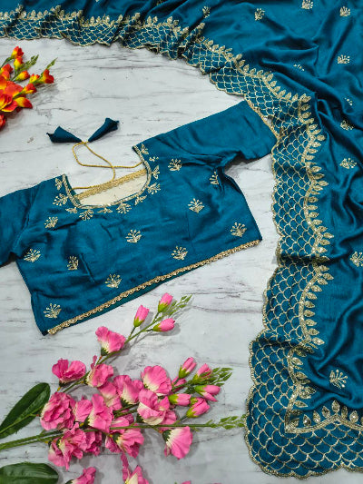 Blue embroidered blouse with matching saree on a wooden surface with pink flowers.