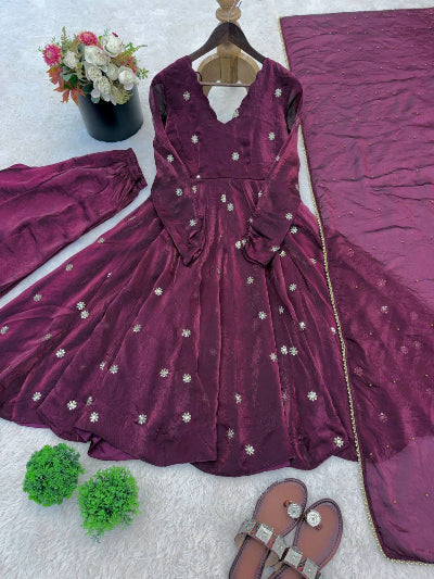 Maroon embroidered dress with matching dupatta on a white surface, accompanied by sandals and flowers.