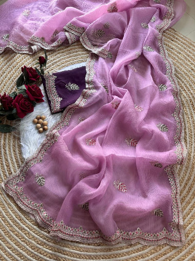 Pink saree with intricate embroidery on a textured surface with flowers and a pillow.