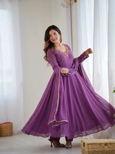 Woman wearing a purple traditional outfit with gold details in a bright room.