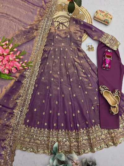 Purple embroidered outfit with gold details, shoes, and flowers on a light gray background