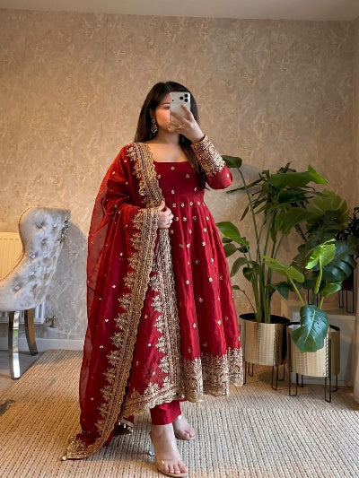 Woman taking a mirror selfie wearing a red traditional outfit with gold embroidery in a home setting.