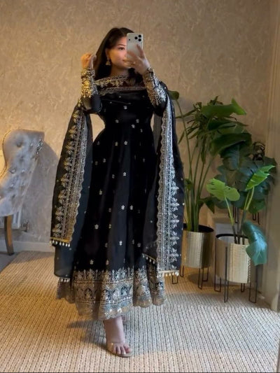 Person wearing a black dress with white patterns in a room with plants and furniture.