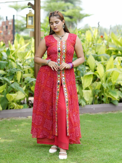 A woman wearing a red and pink patterned kurta with colorful embroidered details down the front, standing outdoors on a green lawn with plants in the background.