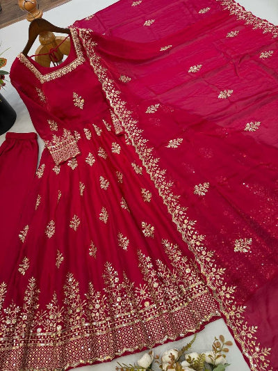 A deep magenta red anarkali dress set with intricate gold embroidery, displayed on a hanger with matching pants and a dupatta on a light surface.