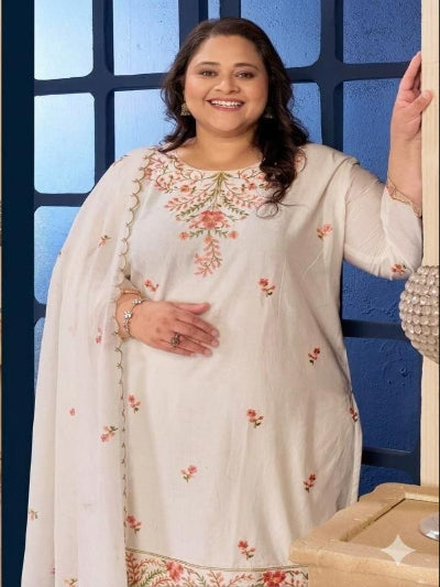 Woman wearing a white embroidered traditional outfit in a room with a blue wall.