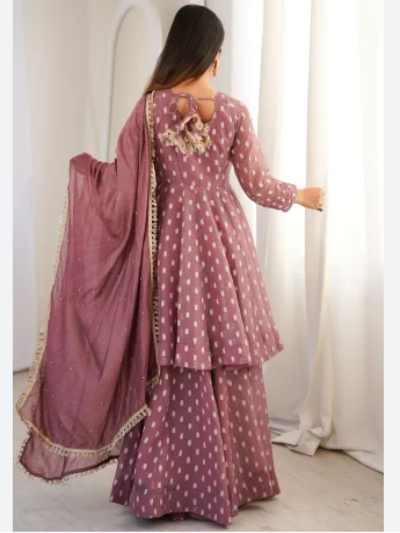 A woman wearing a dusty rose pink three-piece salwar kameez set with white polka dots, shown from the back. The set includes a long-sleeved kurta with floral embroidery on the back neckline, matching flared pants, and a draped dupatta with gold zari borders.