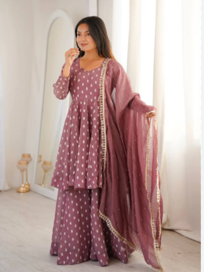 A woman models a traditional three-piece salwar kameez suit in dusty mauve with white polka dots and gold zari embroidery, including a long kurta, matching flared pants, and a sheer dupatta.