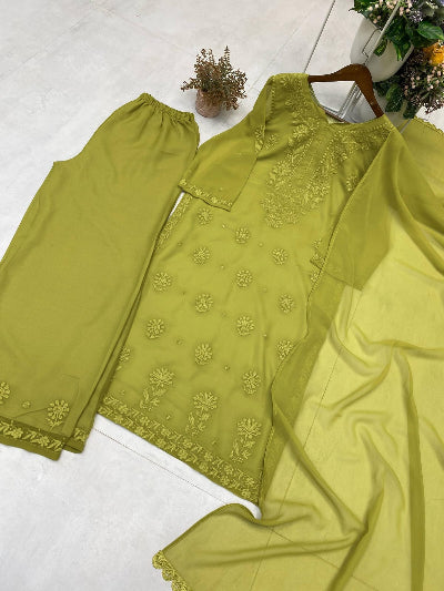 Green embroidered fabric on a white surface with a plant in the background