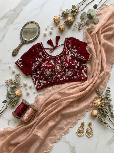 Red embroidered blouse with floral patterns on a marble surface with decorative elements.