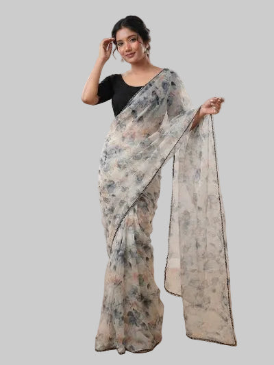 A woman modeling a semi-sheer floral print saree with a black blouse in a studio setting with wooden floors and soft lighting.