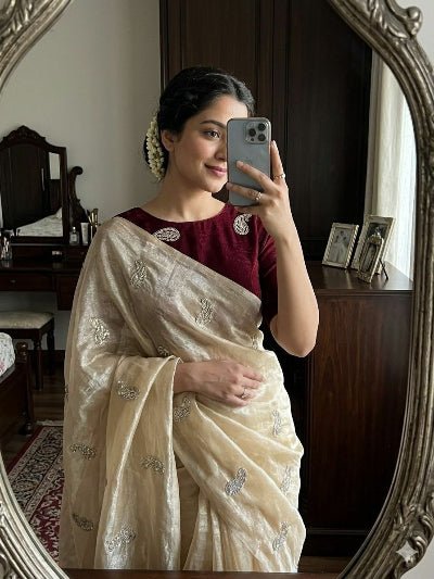 Woman taking a mirror selfie wearing a white saree with a maroon blouse.