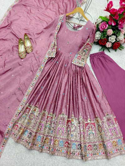 Pink embroidered traditional outfit with a hanger, shoes, and flowers on a pink fabric background