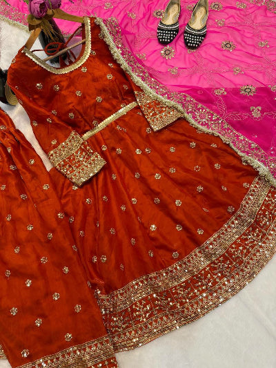 Red embroidered traditional outfit with gold details on a pink fabric background