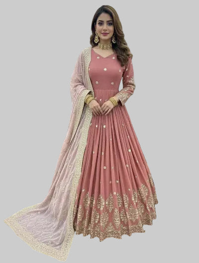 Woman in a pink traditional outfit with gold embroidery in an indoor setting.