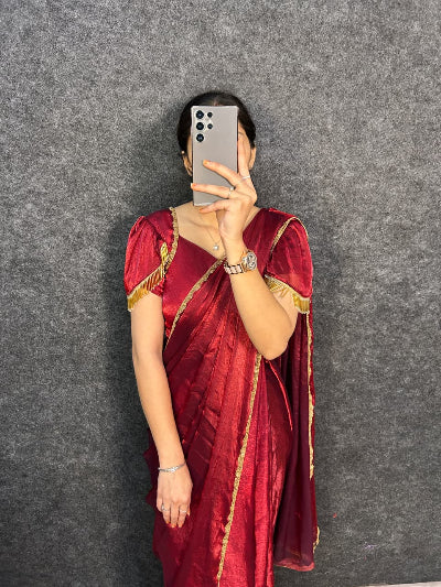 Person wearing a red saree with gold borders against a gray background