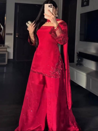 Person wearing a red traditional outfit with intricate designs in a room.