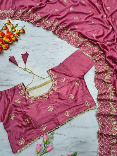 Pink blouse with gold embroidery on a marble surface with flowers.