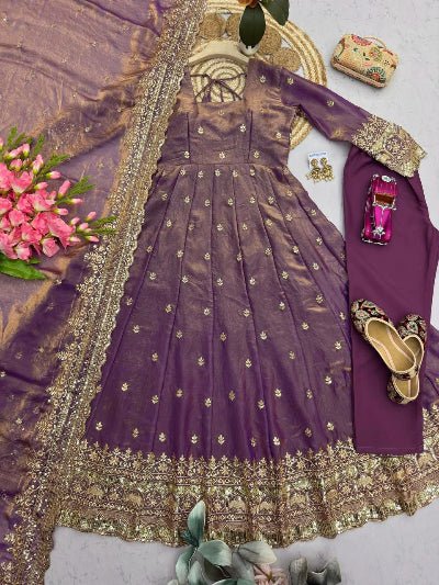 Purple embroidered outfit with gold details, shoes, and flowers on a light gray background