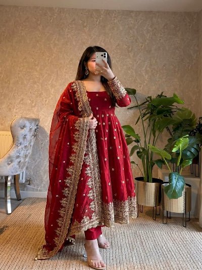 Woman taking a mirror selfie wearing a red traditional outfit with gold embroidery in a home setting.